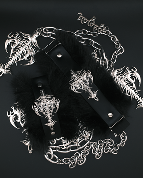 Black faux-fur cuffs with black leather straps and silver-toned metal hardware, decorated with gothic skeleton key and chain motifs, arranged on a dark background.